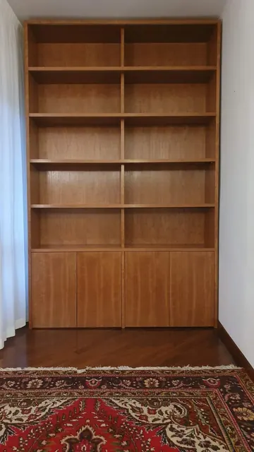 Libreria a parete in legno, con ripiani e quattro ante in basso, in un corridoio